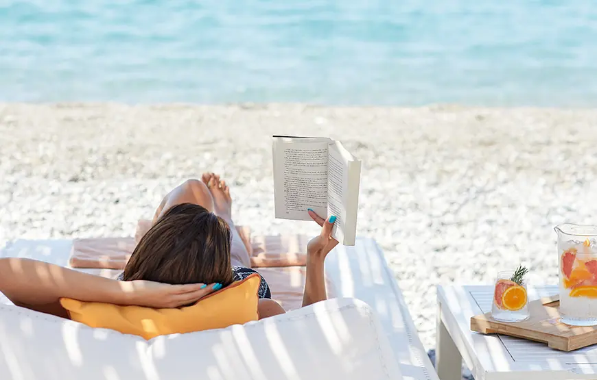 una-donna-è-sdraiata-fronte-mare-sulla-spiaggia-e-ha-in-mano-un-libro