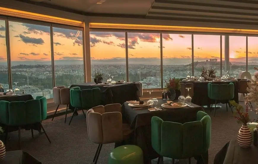 vista-panoramica-dall-interno-di-un-ristorante-con-poltroncine-e-tavoli-apparecchiati-per-mezzo-di-una-parete-a-vetrata-con-tramonto-fuori-su-atene